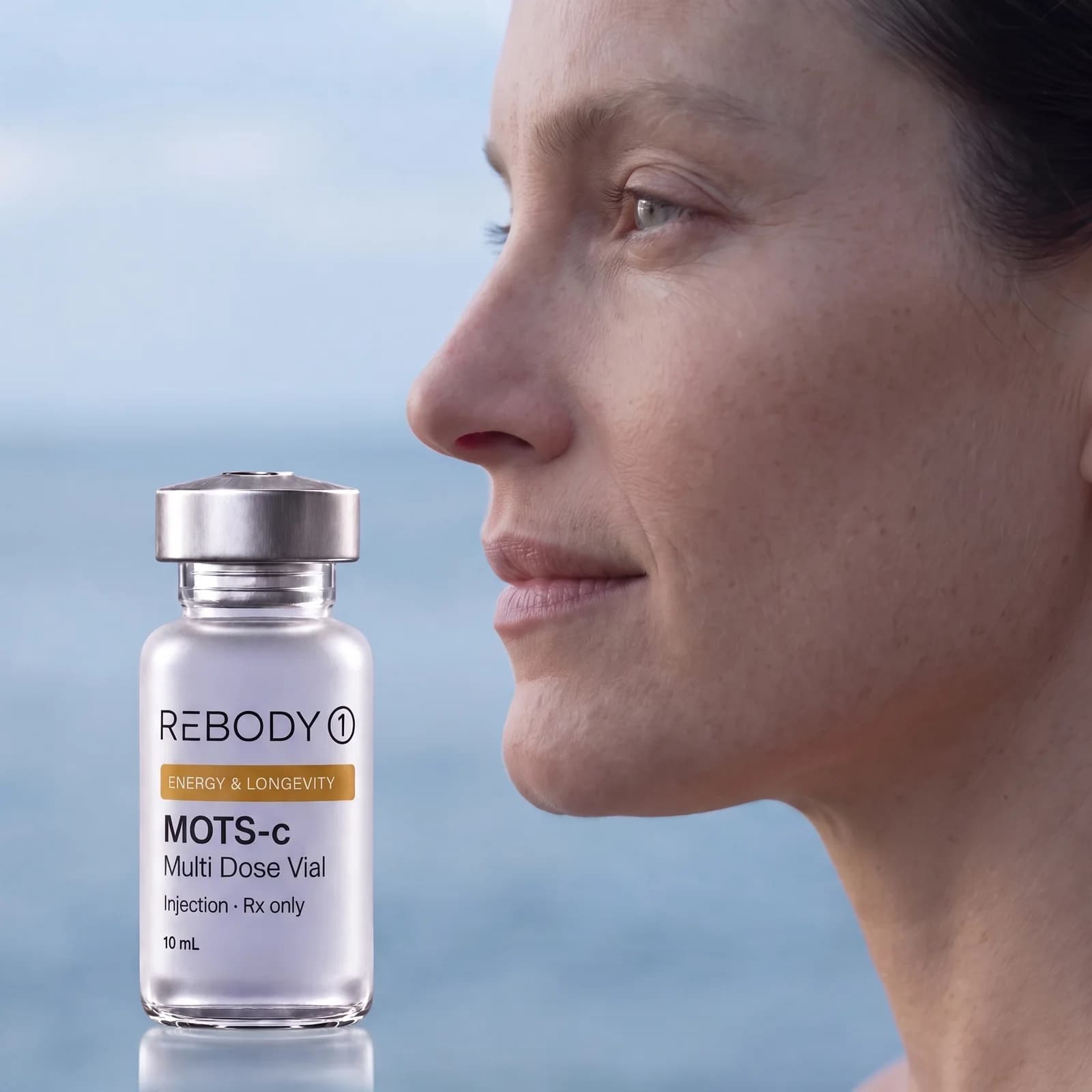 A woman in profile by a misty sea beside a MOTS-c vial